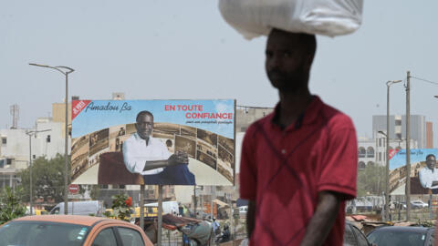 A man walks near an electoral billboard of Senegalese presidential candidate Amadou Ba in Dakar on March 19, 2024.