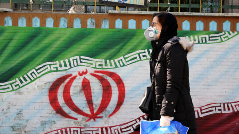 امرأة إيرانية تضع كمامة تسير قرب جدارية لعلم بلادها في طهران في 4 مارس/آذار 2020. 