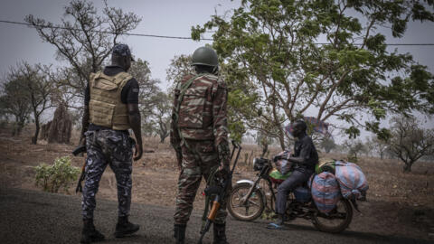 A file photo showing a police officer and a soldier from Benin stopping a motorcyclist at a checkpoint outside Porga, Benin, March 26, 2022.