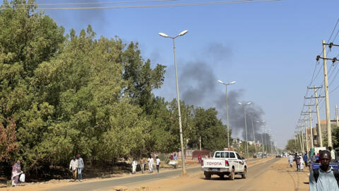 نازحون بسبب الصراع في السودان يسيرون على طول الطريق بينما يتصاعد الدخان على مسافة خلال اشتباكات في ود مدني، عاصمة ولاية الجزيرة، في 16 ديسمبر 2023.