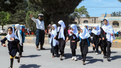 An Afghan policeman stops traffic as schoolgirls cross a road outside a school in Herat on April 16, 2024.