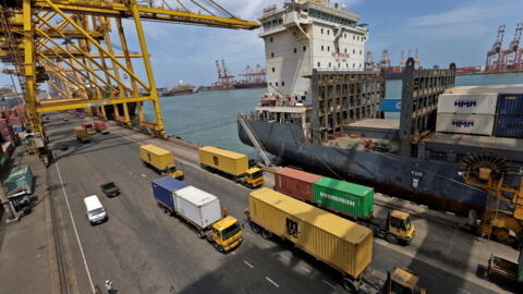 Des camions porte-conteneurs transportent des boîtes à conteneurs devant des conteneurs maritimes au principal port de Colombo au Sri Lanka.