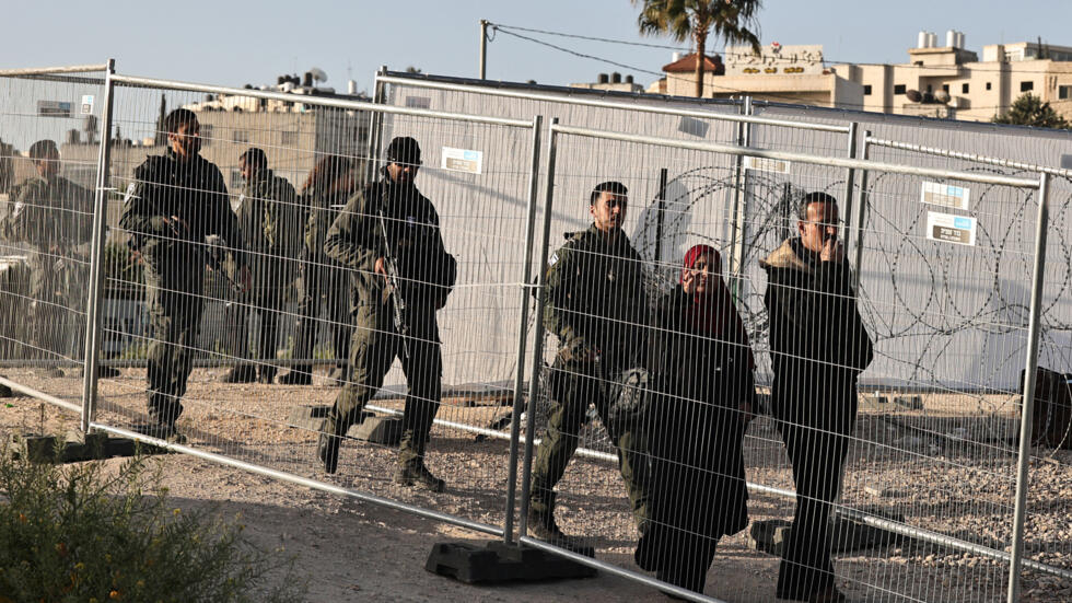 جنود إسرائيليون يشاهدون امرأة تسير بالقرب من حاجز قلنديا في الضفة الغربية المحتلة، 5 أبريل 2024.