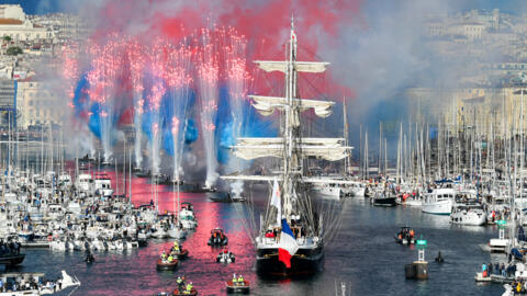 Fireworks go off as a three-mast ship carrying the Olympic flame sails into Marseille's Old Port on May 8, 2024. 