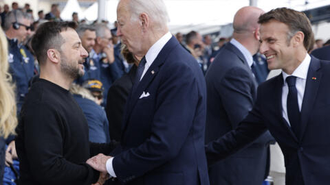 الرئيس الأمريكي جو بايدن يصافح الرئيس الأوكراني فولوديمير زيلينسكي بحضور الرئيس الفرنسي إيمانويل ماكرون خلال احتفالات الذكرى الثمانين لإنزال الورماندي، في 6 حزيران/يونيو 2024.