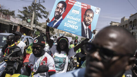 A supporter holds up a poster with presidential candidate Bassirou Diomaye Faye and opposition leader Ousmane Sonko as they march during a campaign on March 10, 2024. 