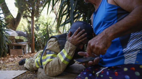 An Israeli firefighter and a resident take cover as sirens warn of rockets launched from southern Lebanon, in Kiryat Shmona, northern Israel