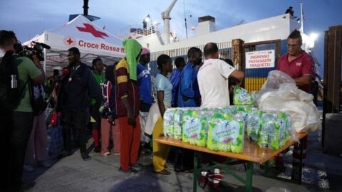 Membros da Cruz Vermelha Italiana distribuem garrafas de água e comida aos migrantes antes de embarcarem num barco para serem transportados para outras cidades, na ilha italiana de Lampedusa. Em 18 de setembro de 2023. 