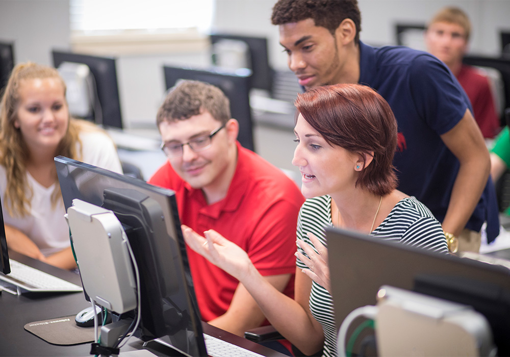 Students gathered around a computer discussing what is on the screen.