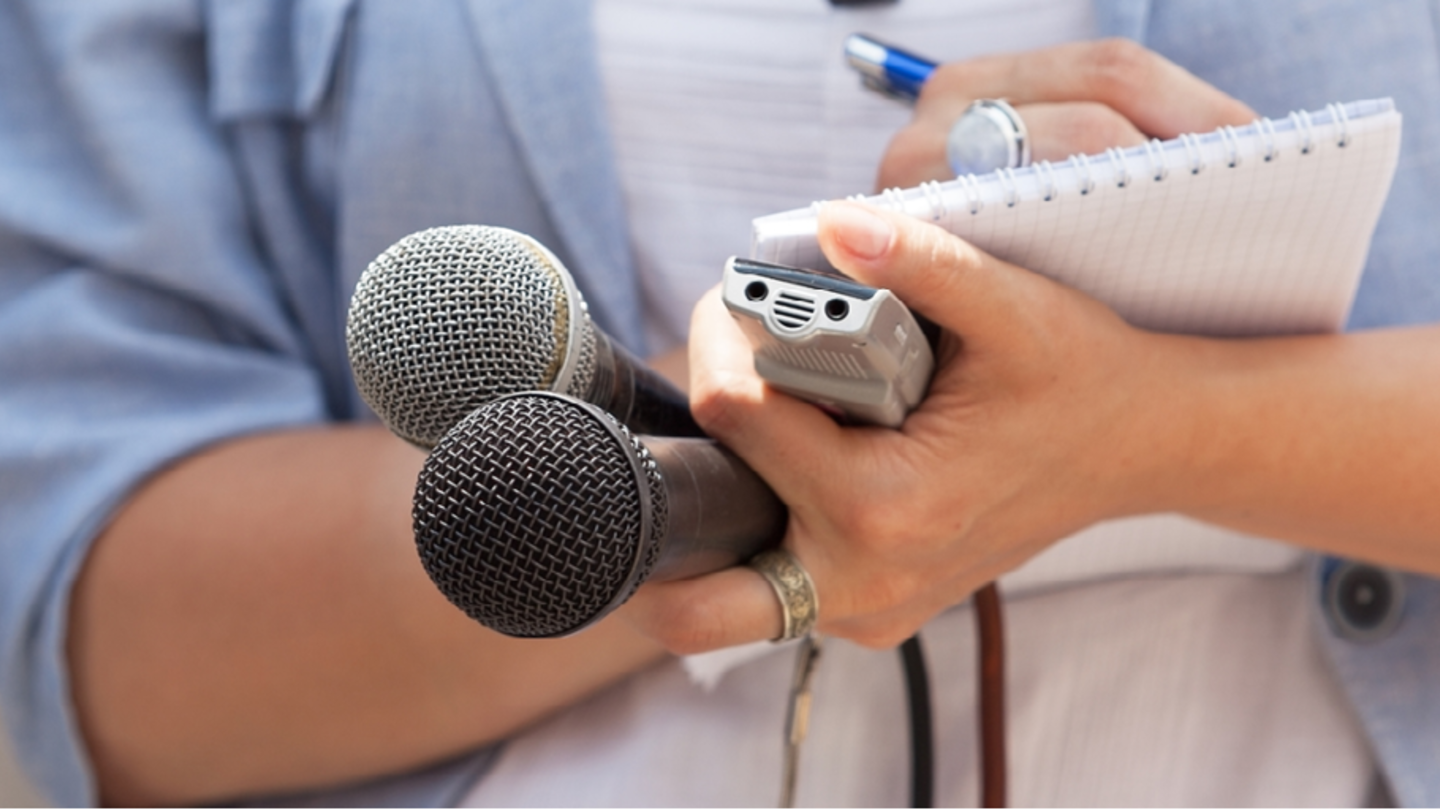 A woman writing notes in a pad holding different microphones