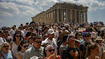 Atop the Acropolis ancient hill, tourists visit the Parthenon temple, background, in Athens, Greece