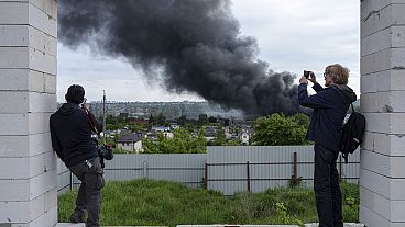 Jornalistas estrangeiros fazem uma reportagem a partir de um ponto de observação enquanto se levanta fumo após um ataque russo em Kharkiv, na Ucrânia, na sexta-feira, 17 de maio de 2024.