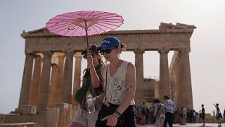 Atina'nın merkezindeki antik Akropolis'te bulunan Parthenon'un önünde yürüyen şemsiyeli turistler, 12 Haziran 2024. 