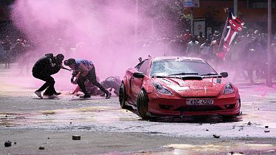 Manifestanti per le strade di Nariobi si riparano dagli idranti della polizia durante la protesta contro la nuova legge finanziaria