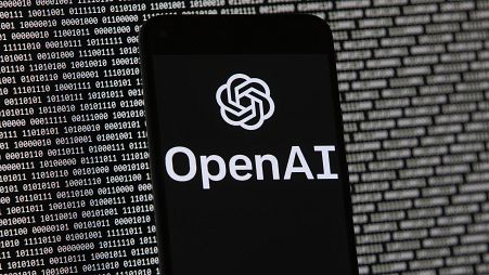 The OpenAI logo appears on a mobile phone in front of a computer screen with random binary data, Thursday, March 9, 2023, in Boston. 