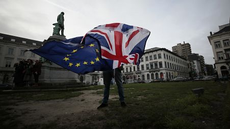 Peter Cook, apoiante pró-UE, desfralda uma bandeira da União e da UE antes de uma cerimónia para celebrar a amizade entre o Reino Unido e a UE, em frente ao Parlamento Europeu, em Bruxelas.