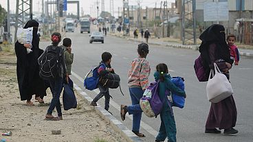 أطفال في غزة يعبرون الطريق وهم يحملون متاعا قليلا أجبروا على النزوح بسبب القصف الإسرائيلي