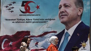 Турецкие женщины и ребенок идут перед плакатом президента Реджепа Тайипа Эрдогана после военного парада на северном Кипре, 20 июля 2024 года