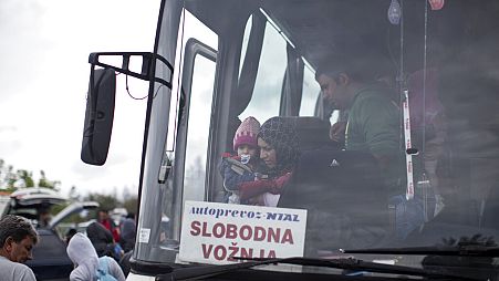 A woman carries a child as she exits a bus that transported her to Serbia's border with Croatia in Berkasovo, Serbia, Sunday, Sept. 27, 2015.