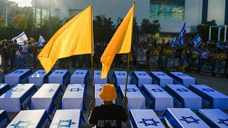 A man holds flags next to mock coffins covered Israeli flags representing the 27 hostages