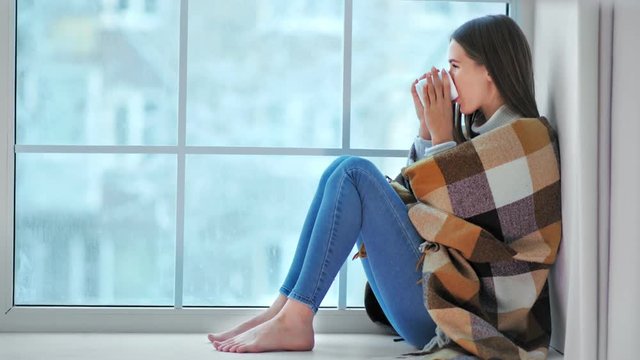 Smiling barefoot woman sitting on windowsill looking on winter weather