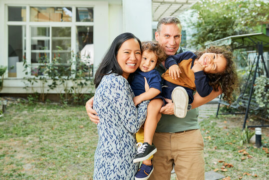 Father, mother and two kids standing in backyard of their house, smiling, laughing and looking at camera