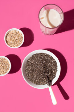 Semillas de chía y semillas de sésamo con un vaso de leche de avena sobre fondo rosa. Vista superior