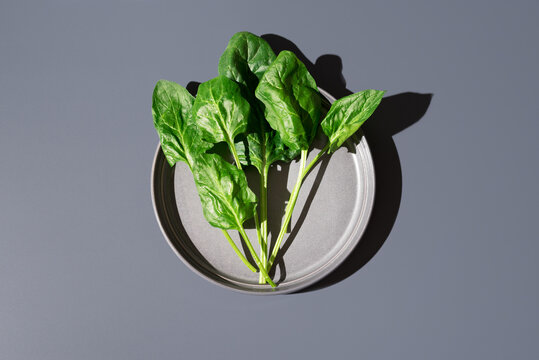 Hojas de espinacas frescas sobre un plato gris sobre fondo gris. Vista superior