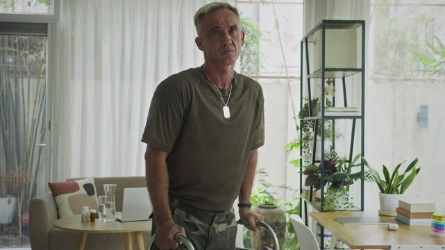 Tilt up portrait of injured male ex-soldier in camouflage rehabilitating at home with help of walker