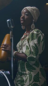 Vertical view of Black young woman singing and playing guiro during rehearsal in bar