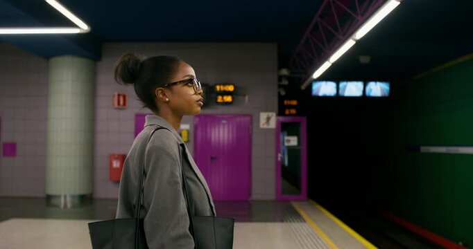 A woman in formal clothes is waiting for a train standing on a subway platform. Side view