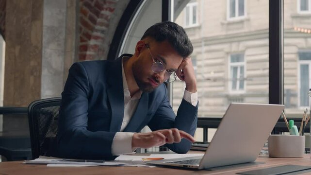 Tired stressed sad male guy Arabian man office employee tap keyboard on laptop boring online work in office alone Indian businessman exhausted lazy burnout overwork headache stress business problem