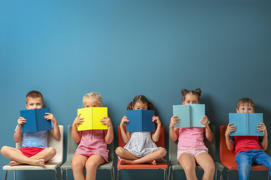 Cute little children reading books while sitting near color wall