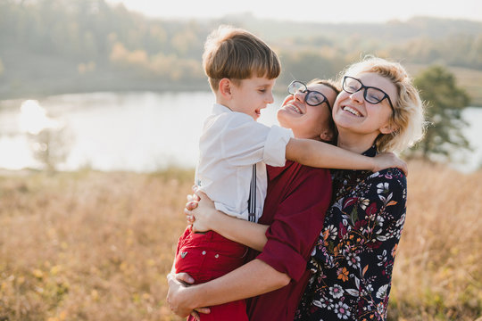 Samesex caucasian lesbian family with a child and a dog walking outdoors on the background of beautiful nature. Mothers having fun with their son.