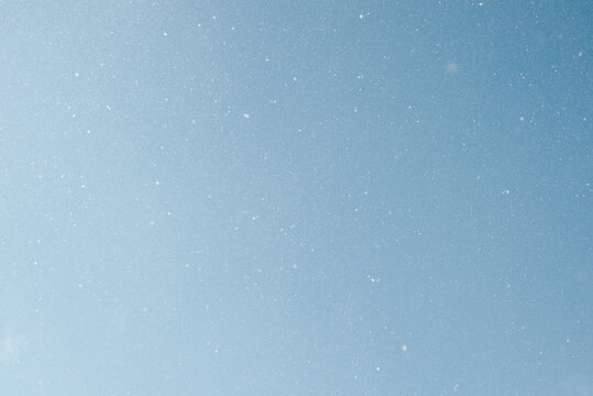 Falling snow, white snowflakes on clear blue sky outdoors. Defocus light slow snowfall in winter