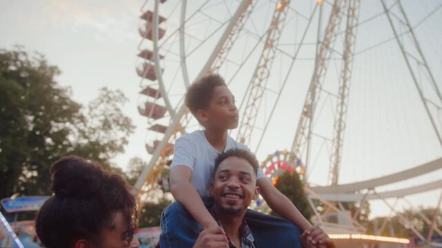 Man giving son piggyback ride while passing by ferris wheel