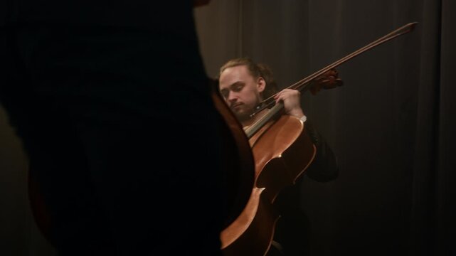 Medium shot of young Caucasian string quartet wearing elegant suits and dresses with violins, bass and cello in hands taking their seats and preparing to play on stage