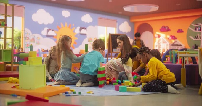 Creative Multiethnic Friends Playing in Kindergarten Together with Female Pedagogue. Boys and Girls Constructing a House Out of Colorful Building Blocks. Children Having Fun in Modern Daycare Center