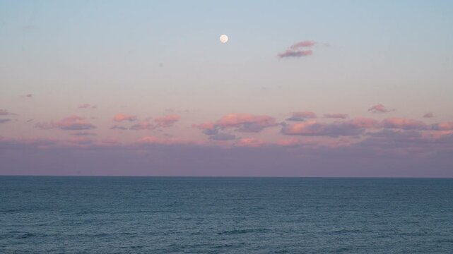 Medium shot of the moon and sunset over the Atlantic Ocean on Carolina Beach, NC.