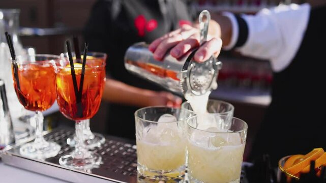 Bartender working, beautiful row line of different coloured liquor alcohol cocktails on a open air party in a bar, and others on catering banquet on event, barman mixing drinks and beverages in club