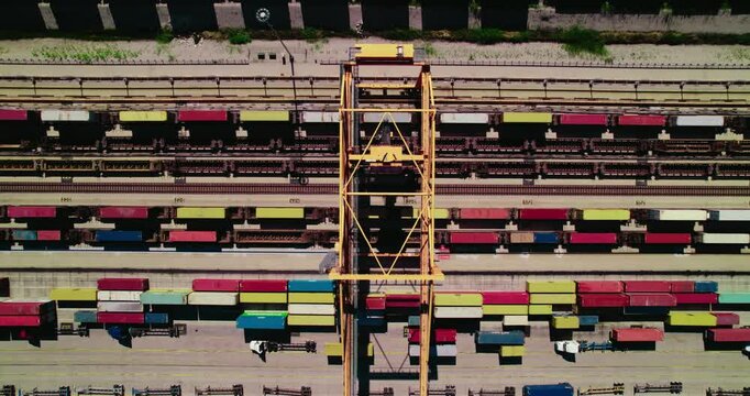 Aerial perspective centered on a towering yellow gantry crane, overlooking a vibrant tapestry of colorful shipping containers and multiple rail tracks.