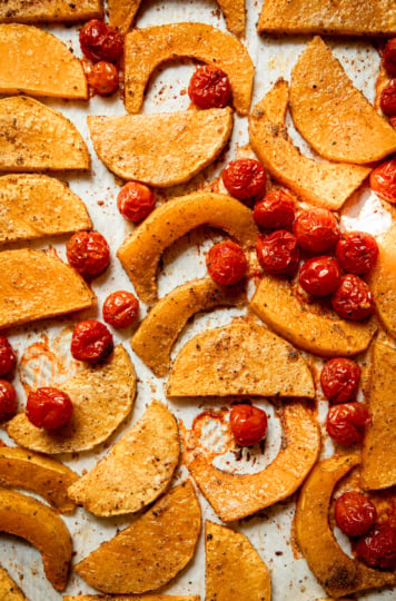 An overhead shot shows roasted slices of butternut squash and burst cherry tomatoes on a sheetpan.