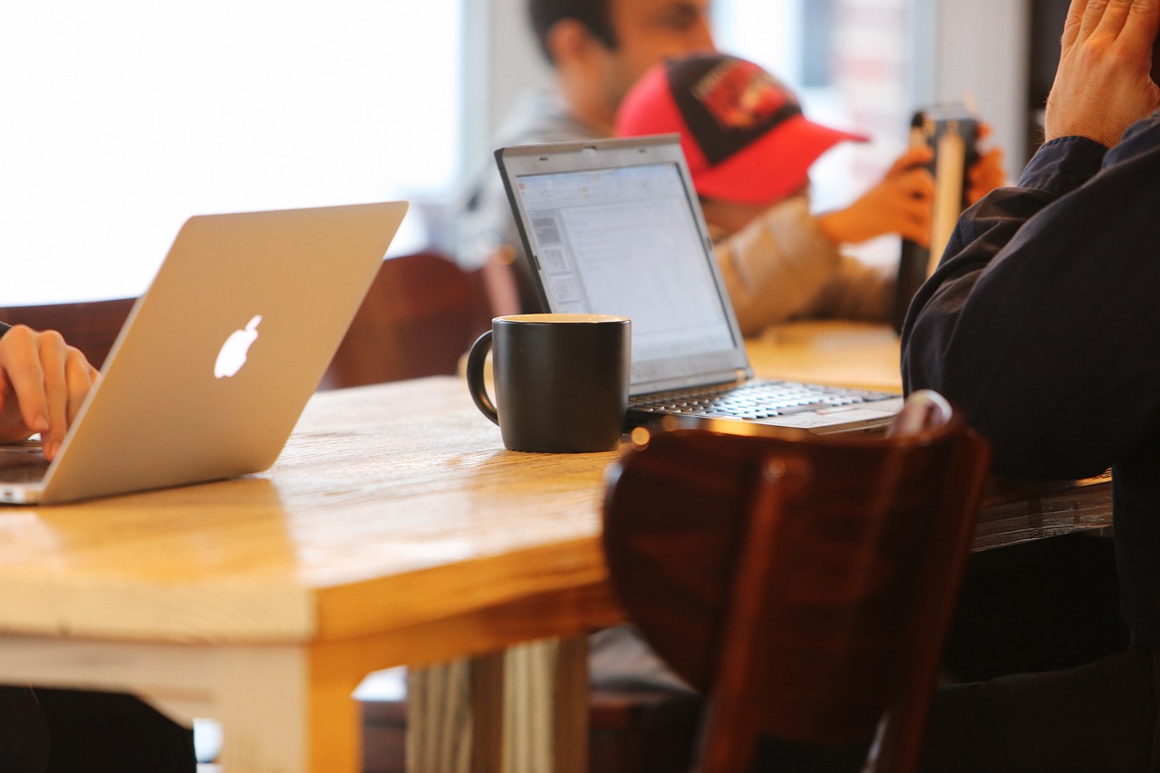 A laptop and mug resting on a desk in front of a person's arm