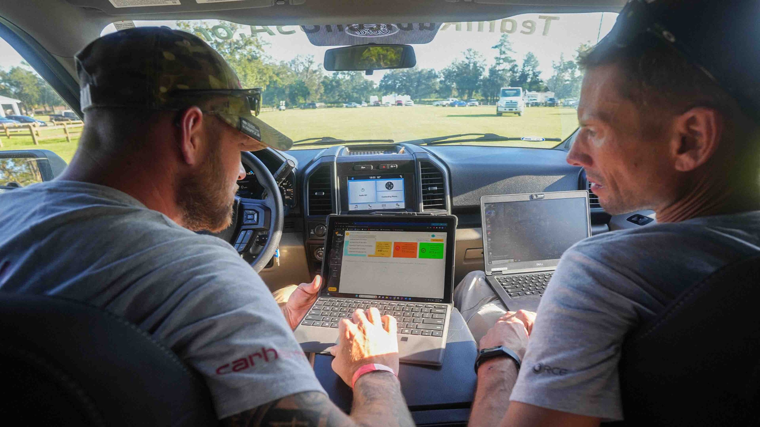 Two men sitting in the back seat of a car using laptops.