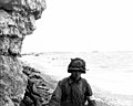 A medic of the 3d Bn., 16th Inf. Regt., 1st U.S. Inf. Div., moves along a narrow strip of Omaha Beach administering first aid to men wounded in the landing