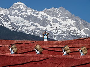 #4: Mulheres do grupo étnico naxi carregando cestos; cena de uma apresentação pública no teatro ao ar livre da Montanha Nevada do Dragão de Jade. Lijiang, província de Yunnan, China. – Atribuição: CEphoto, Uwe Aranas / Cccefalon (CC BY-SA 3.0)