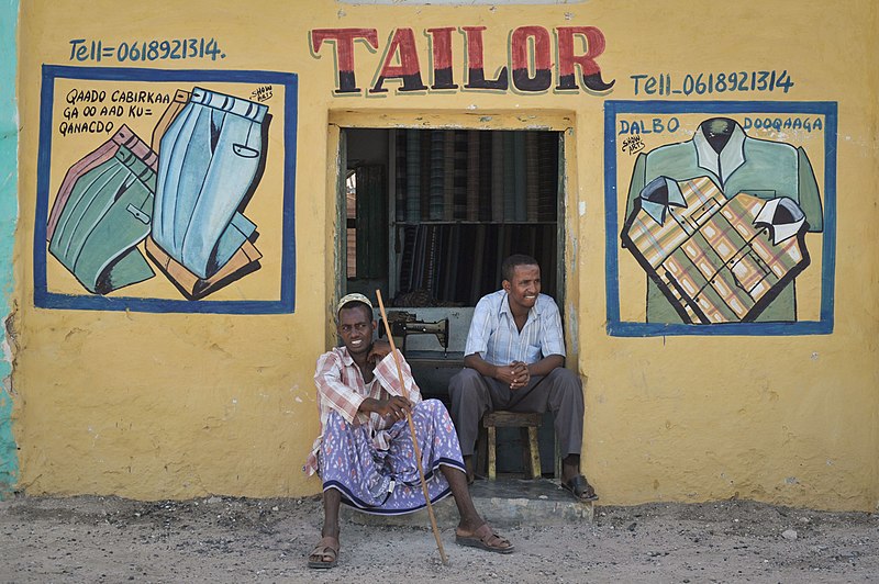 File:Two men sit outside of their shop in Qoryooley, Somalia, as African Union forces pass by their shop in a routine foot patrol on April 29. Captured just over one month ago from al Shabab extremists, (14101106483).jpg
