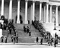 Body bearers carrying the casket of President Kennedy up the center steps of the United States Capitol Building, followed by a color guard holding the flag of the President of the United States, and the late President's widow, Jacqueline Kennedy and her children, Caroline Kennedy and John F. Kennedy, Jr. on November 24, 1963.