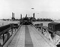 Floating causeway of the "Mulberry" artificial harbor off "Omaha" Beach, 16 June 1944, with a half-track rolling toward the shore. Note tugs nested beside the pierhead in the background.