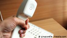 Eine Hand hält einen Telefonhörer, darunter ein größeres Telefongerät (© sinuswelle, Fotolia.com)